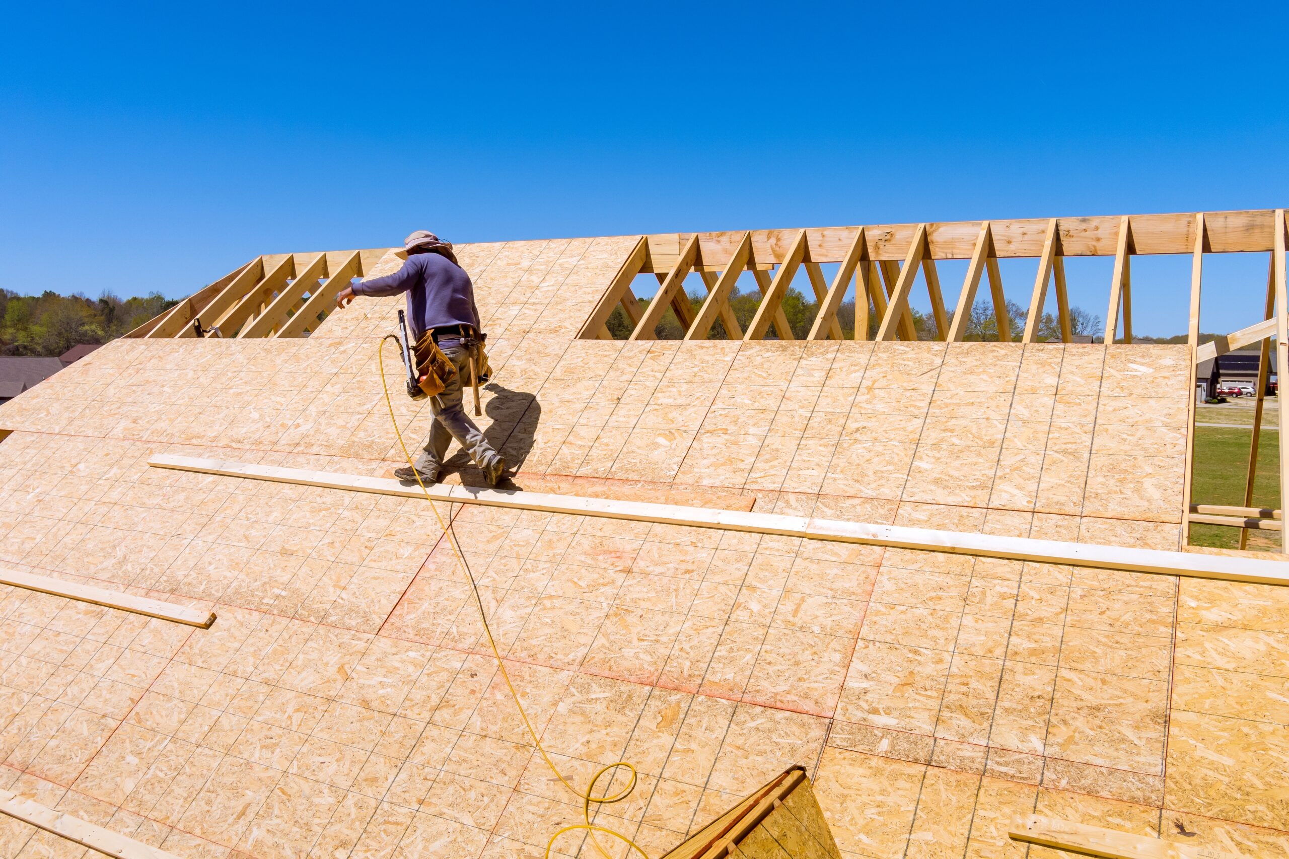 Roofer installing plywood panel on new roof construction, assessing roof condition for replacement.