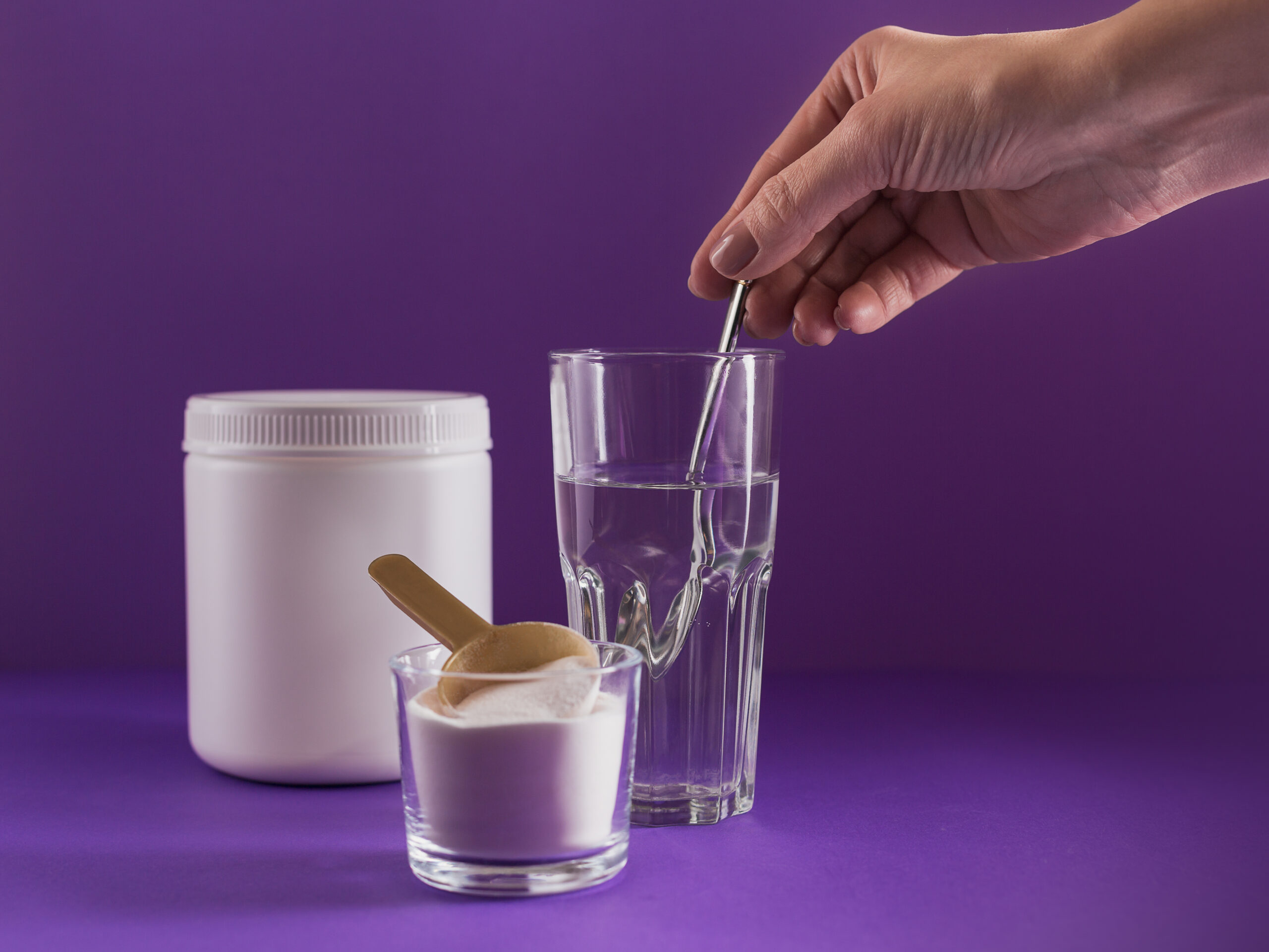 Glass of water with dissolved collagen and electrolyte powder, alongside a container and spoon.